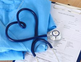 Medical stethoscope twisted in heart shape lying on patient medical history list and blue doctor uniform closeup. Medical help or insurance concept. Cardiology care health protection and prevention