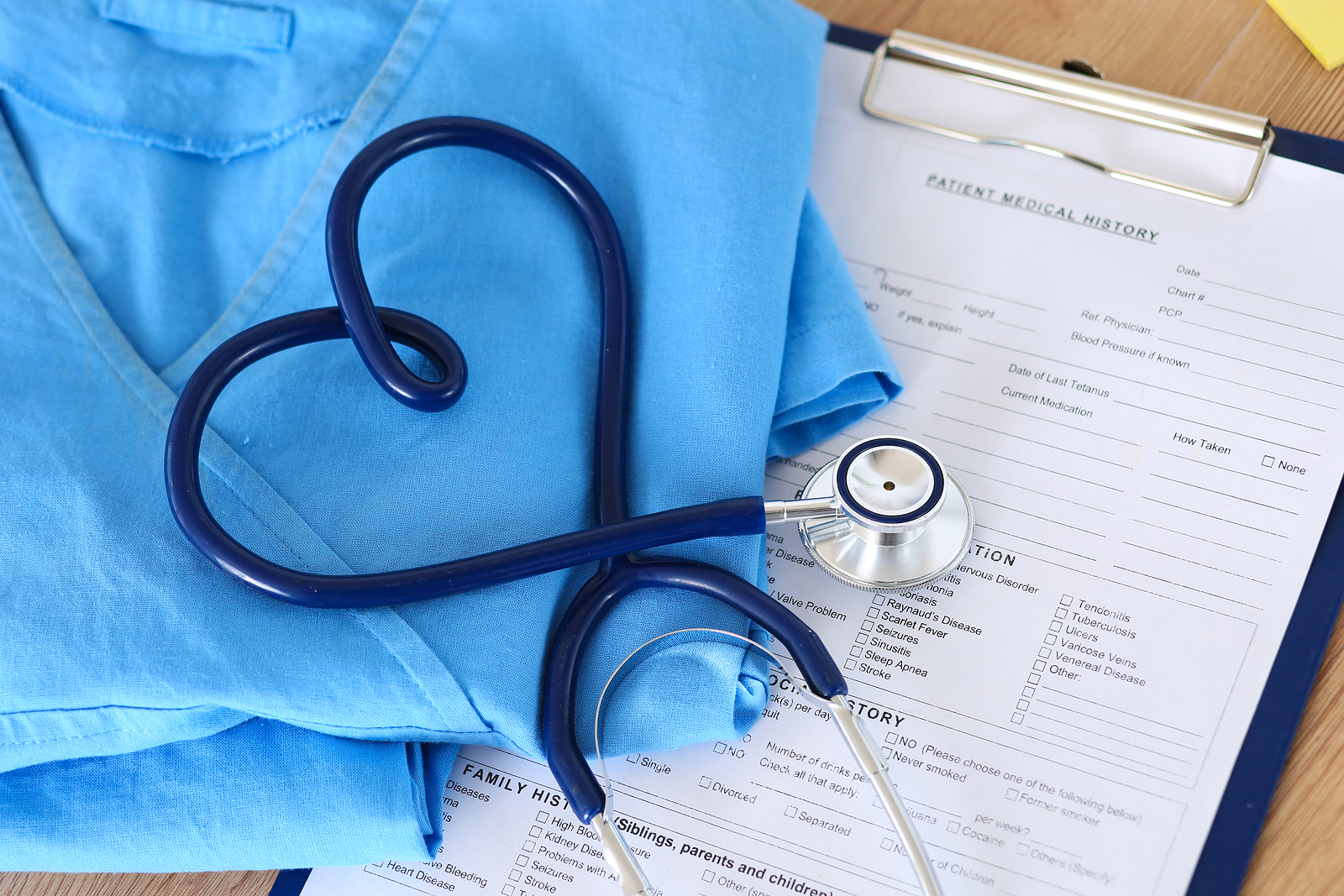 Medical stethoscope twisted in heart shape lying on patient medical history list and blue doctor uniform closeup. Medical help or insurance concept. Cardiology care health protection and prevention