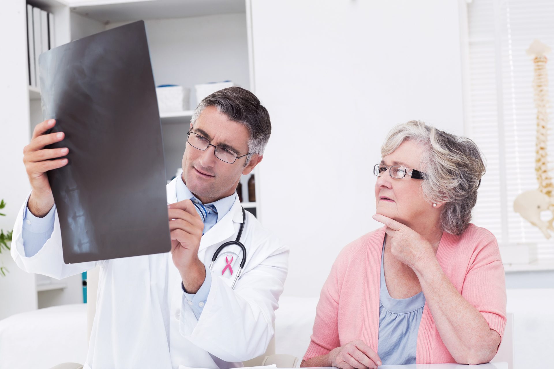 Pink awareness ribbon against doctor explaining x-ray to female patient